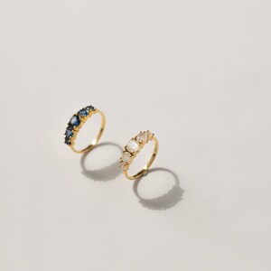 May include: Two gold rings with gemstones. One ring has blue gemstones and the other has white gemstones.