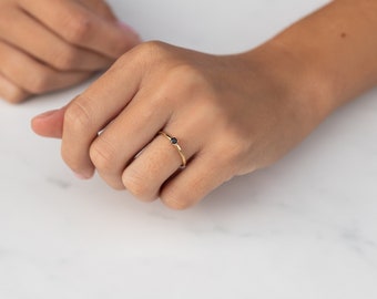 May include: A simple gold band ring with a small black gemstone.