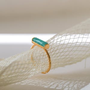 Könnte beinhalten: Ein goldener Ring mit einem rechteckigen, hellgrünen Stein, der in die Band eingefasst ist.