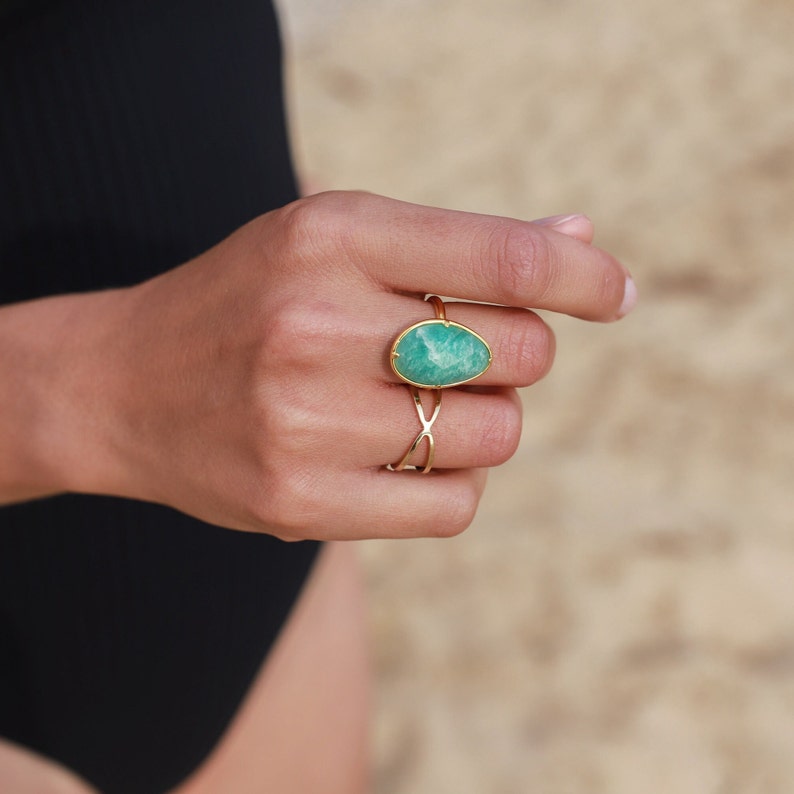 May include: A gold ring featuring a large, oval-shaped green gemstone. The ring is worn on a finger.