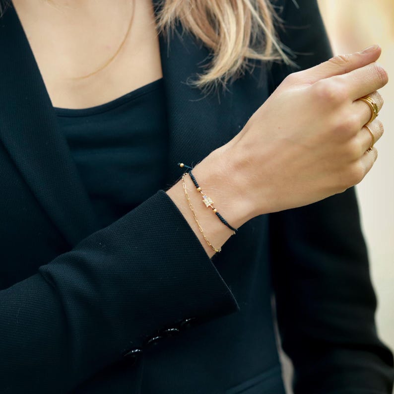 May include: A black string bracelet with a gold star charm and a gold chain bracelet. The bracelets are worn on a person's wrist.