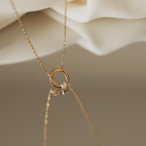 Puede incluir: Un collar de cadena de oro con un delicado colgante circular con una pequeña piedra preciosa transparente.