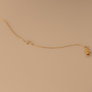 Op de afbeelding: Een delicate goudkleurige ketting met een kleine kruisvormige hanger versierd met sprankelende edelstenen. De ketting heeft een fijne ketting en een karabijnsluiting. De sieraden worden gepresenteerd tegen een neutrale achtergrond.