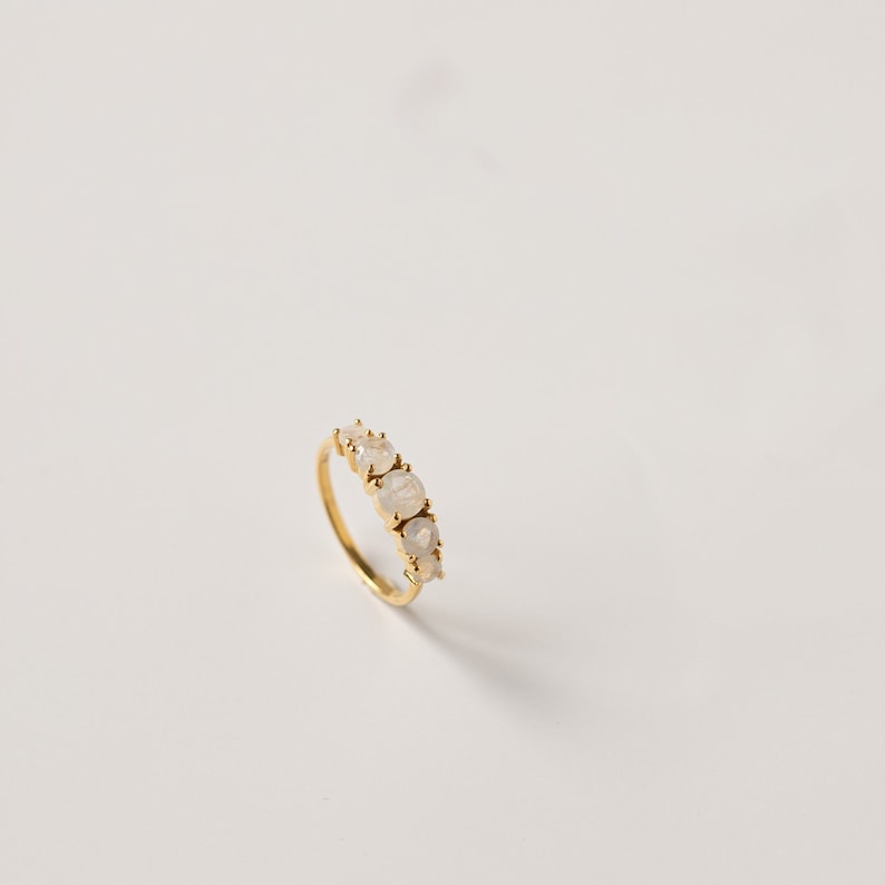 May include: A gold ring with five white moonstone gemstones set in a row.