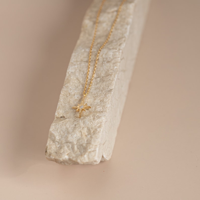 Puede incluir: Un collar de cadena dorada con un peque&ntilde;o colgante de estrella con una sola piedra transparente en el centro.