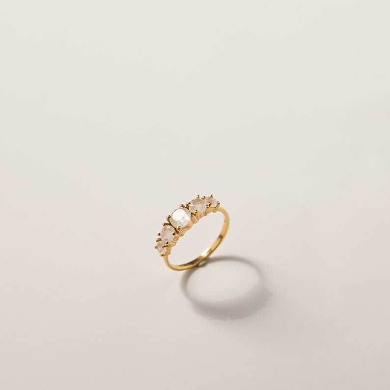 May include: A gold ring with five oval-shaped moonstone gemstones set in a band.