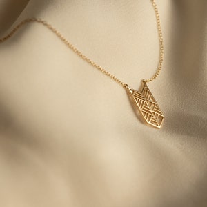 Puede incluir: Un collar de oro con un colgante geométrico. El colgante es un diseño grande y calado con forma triangular.
