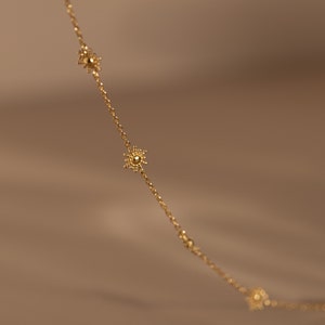 Puede incluir: Un collar de cadena dorada con pequeños abalorios en forma de flor delicados.