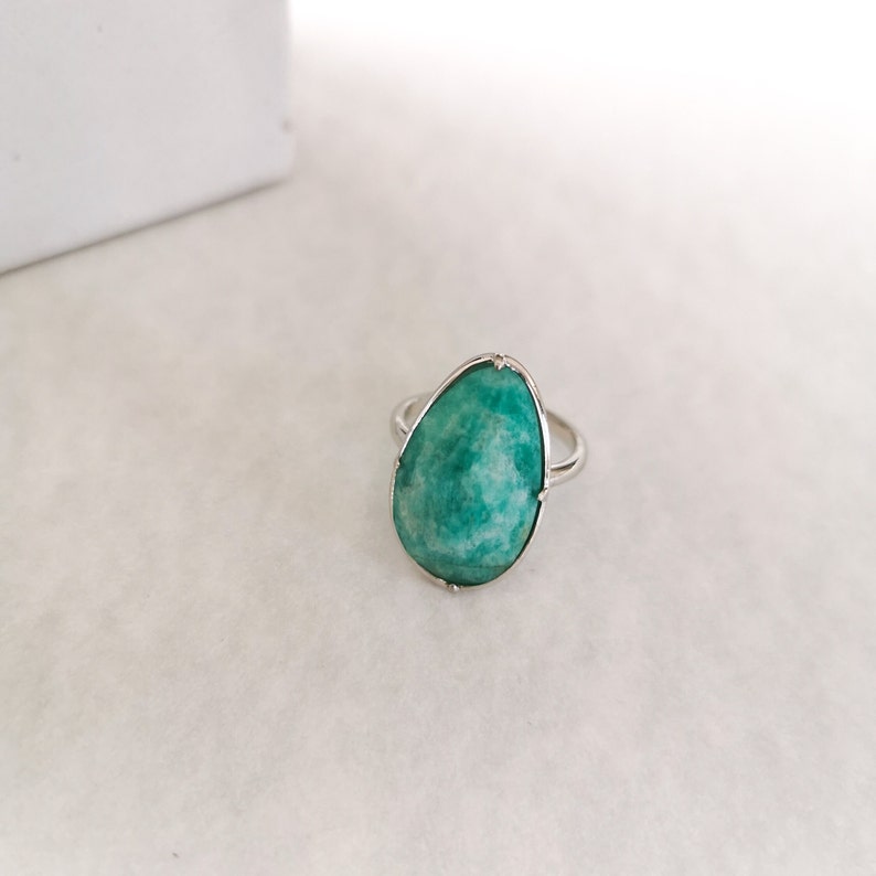 May include: A silver ring featuring a large, teardrop-shaped green gemstone.