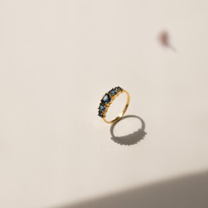 May include: A gold band ring with a row of blue oval-shaped gemstones.