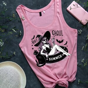 May include: Pink tank top with a graphic of a witch in a witch hat, sunglasses, and a black cat, floating in a pool with the text "Hot Ghoul Summer".
