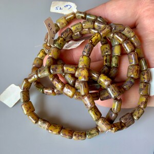 Puede incluir: Primer plano de un montón de cuentas de vidrio amarillas y marrones. Las cuentas son de forma rectangular y tienen un aspecto moteado y manchado. Las cuentas están dispuestas en un montón suelto, y algunas se superponen.