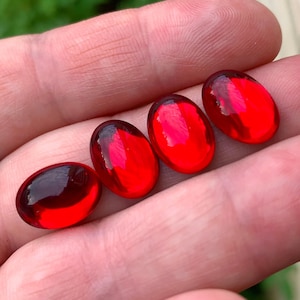 May include: Four oval-shaped, red glass cabochons. The cabochons are smooth and glossy.