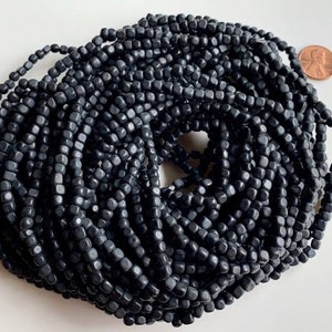 May include: A strand of black square beads, approximately 6mm in size. The beads are made of a matte black material and are strung on a clear thread. The beads are arranged in a circular pattern, with the ends of the strand meeting in the center.