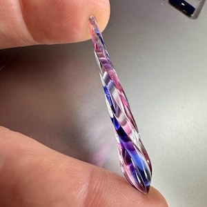 May include: A long, thin, glass pendant with a swirl pattern in shades of pink, blue, and white.
