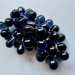 May include: A cluster of dark blue glass grapes, each with a teardrop shape and a glossy finish.