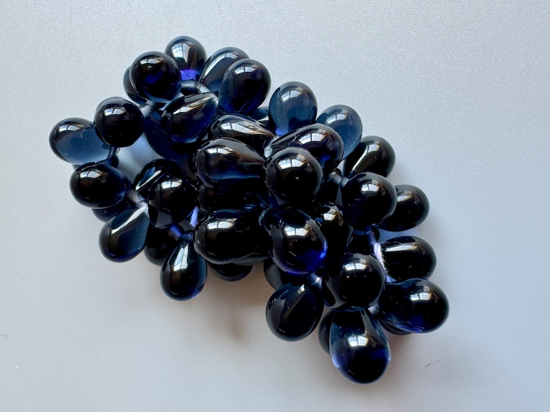 May include: A cluster of dark blue glass grapes, each with a teardrop shape and a glossy finish.