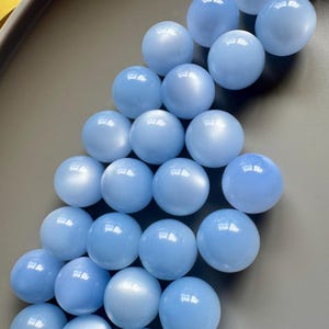 May include: A collection of light blue, spherical beads. The beads have a smooth, glossy surface and are arranged closely together. The color is a soft, pastel blue, and the beads appear to be made of a translucent material.