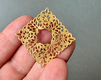 May include: Gold filigree pendant with a square shape and intricate floral designs. The pendant has a large open center.