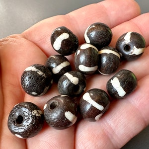 May include: A collection of round, brown wooden beads with white painted stripes. The beads have a hole drilled through the center for stringing.