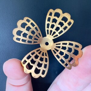 以下が含まれることがあります： 繊細で複雑なデザインの金色の金属製のフラワーモチーフ。花は4枚の花びらで、中央に円形の穴が開いています。