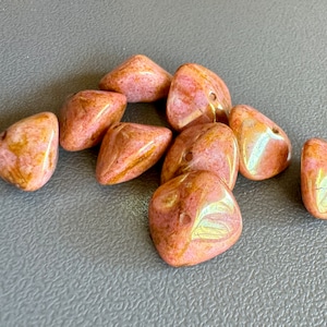 May include: A group of eight pink and brown irregularly shaped beads with a hole in the center of each bead.