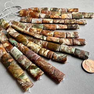 May include: A strand of brown, green, and white patterned rectangular gemstone beads. The beads are approximately 1 inch long and are strung on a white cord.