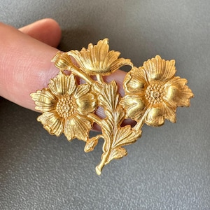 May include: Gold-toned metal flower brooch with three dimensional flowers and leaves.