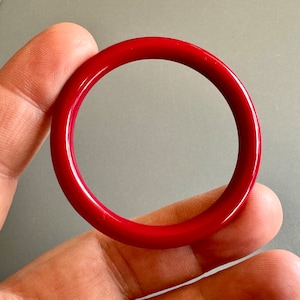 May include: A red bangle bracelet made of smooth, polished plastic.