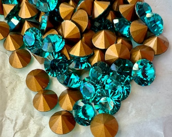 Può includere: Una collezione di strass turchesi e dorati. Gli strass sono sparsi su una superficie bianca.
