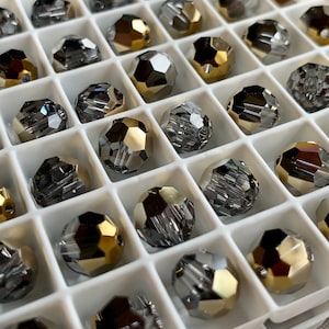 May include: A close-up of a container filled with round, faceted glass beads. The beads are a mix of silver and gold colors.