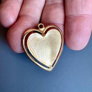 Puede incluir: Un colgante de corazón dorado con un diseño texturizado. El colgante tiene un diseño de doble corazón con un corazón más pequeño dentro de un corazón más grande.