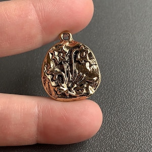 May include: Gold-toned pendant charm featuring a detailed floral design with three stylised flowers. The charm has a textured, slightly rough surface.