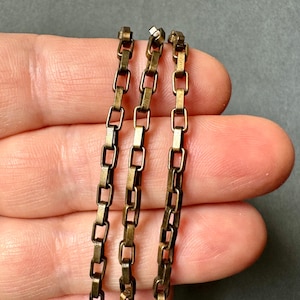 May include: Three strands of gold-toned chain with square links. The chain is made of metal and has a polished finish.