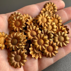 May include: A collection of gold-toned metal sunflower-shaped embellishments. The embellishments are approximately 1 inch in diameter and have a raised, textured design.