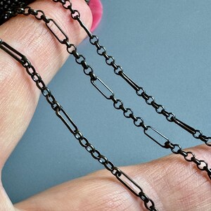 May include: Three black metal chains of different lengths and styles. The chains are made of small, linked ovals and rectangular links.
