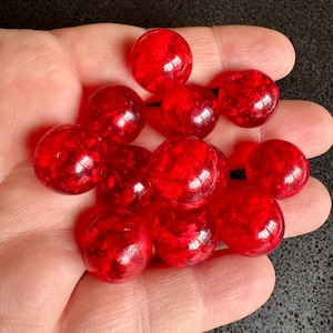 May include: A collection of ten translucent red glass marbles. Each marble has a speckled, crackled appearance. The marbles are held in a hand, with the background out of focus.