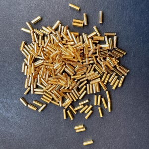 May include: A large pile of gold-colored metal beads, perfect for jewelry making or crafting projects.