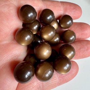 May include: A collection of brown, spherical beads with a glossy finish. The beads vary in shade from light to dark brown, and are smooth and reflective. The beads are clustered together, suggesting they are part of a larger craft or jewelry project.