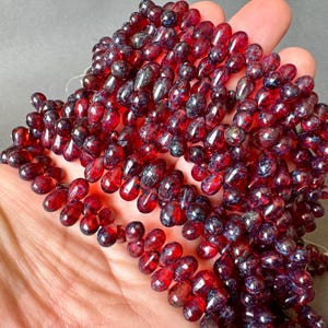 May include: A strand of red and black teardrop-shaped glass beads. The beads have a speckled, iridescent finish.