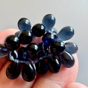 May include: A cluster of dark blue glass beads in a teardrop shape. The beads are strung together on a clear thread.