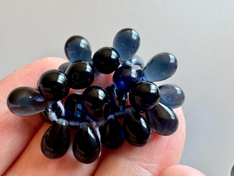 May include: A cluster of dark blue glass beads in a teardrop shape. The beads are strung together on a clear thread.