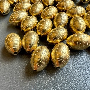 May include: A group of gold-colored oval beads with a textured surface. The beads are arranged in a random pattern on a gray surface.