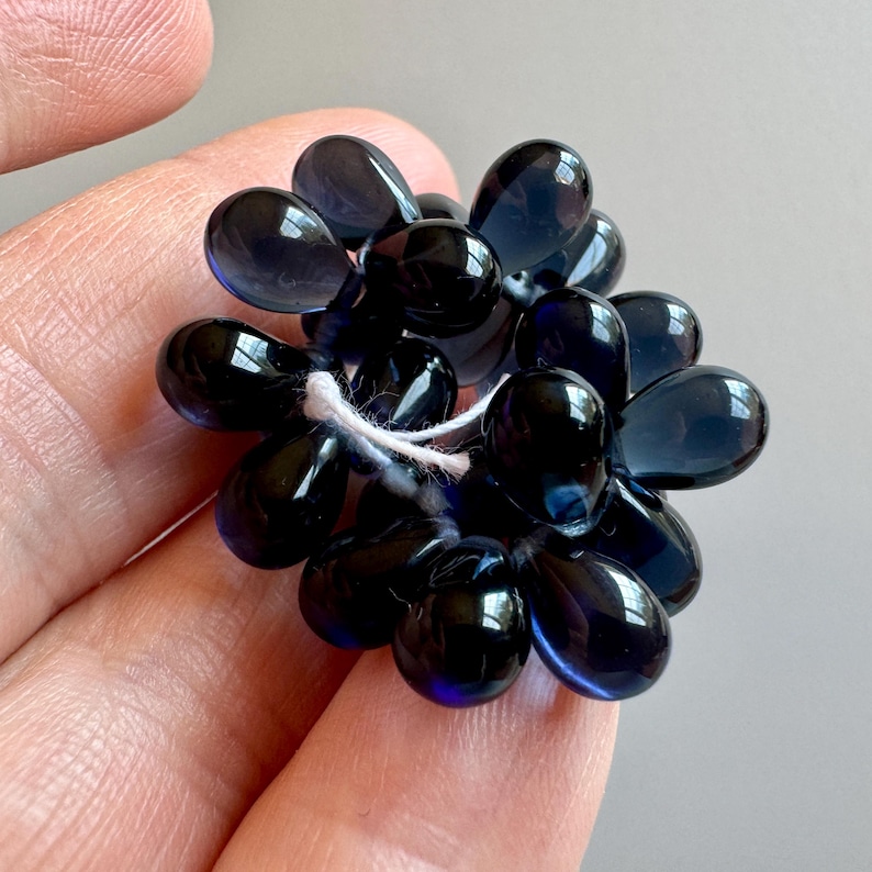 May include: A cluster of dark blue glass beads in a teardrop shape. The beads are strung together with white thread.