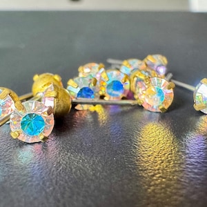 Puede incluir: Un grupo de piedras de cristal iridiscentes con engastes dorados y postes plateados. Las piedras de cristal están dispuestas en un racimo y reflejan la luz.