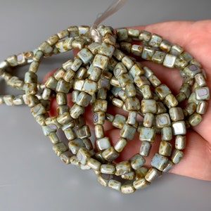 May include: A strand of light green square ceramic beads with brown speckles and white accents.