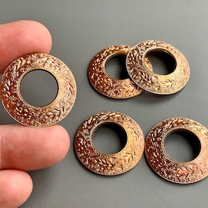 May include: Five gold-toned metal rings with an intricate floral design. The rings have a circular shape with a hole in the center.