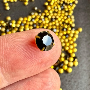 Vintage jet black SS29 chatons (round rhinestones) preset in four pronged, closed back brass settings. Sold per eight pieces. SKU 10627