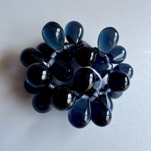 May include: A cluster of dark blue glass beads in the shape of teardrops. The beads are strung together on a clear thread.