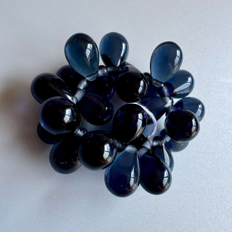 May include: A cluster of dark blue glass beads in the shape of teardrops. The beads are strung together on a clear thread.